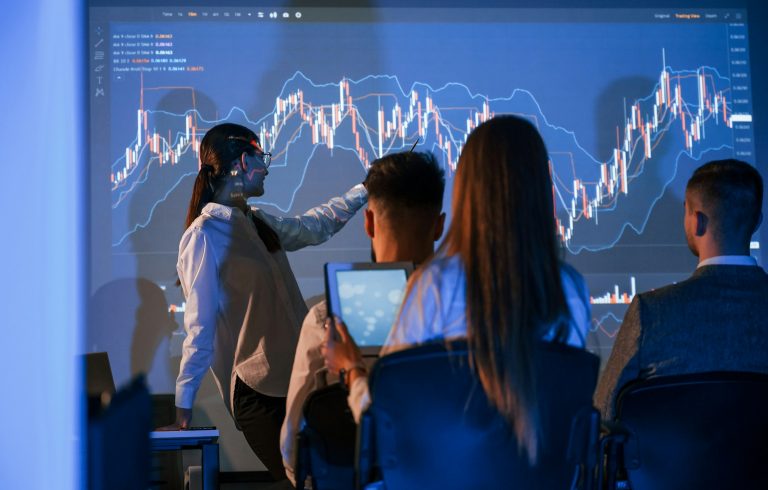 Mitarbeiter in einem Büro hören einer weiblichen Führungskraft zu, die einen Plan auf einem Projektor präsentiert, um die Vorteile der Digitalisierung mit Makemore zu erläutern